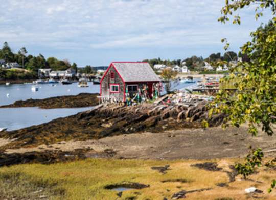 A red building sits on a rocky shore with boats in the water.