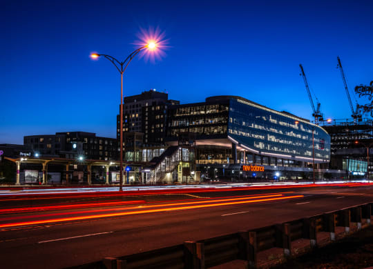 A view of Boston Landing lit up at night with cranes in the background and the Mass Pike in the foreground