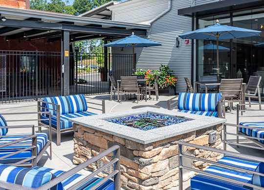 A patio with blue and white striped chairs and a stone fire pit.