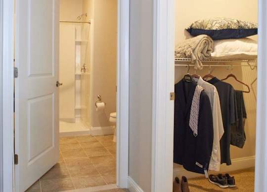 A white door is open to a bedroom with a bed and clothes hanging up.