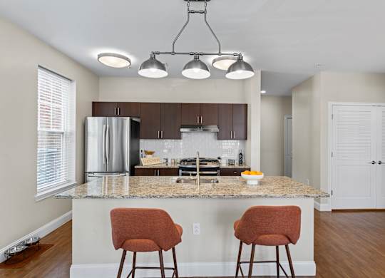 A kitchen with a granite countertop and two chairs.