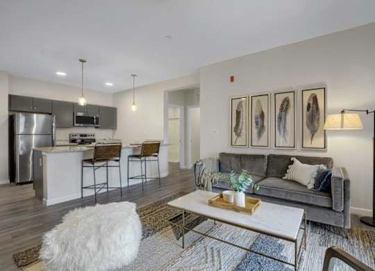 A modern living room with a grey couch, a white coffee table, and a kitchen area in the background.