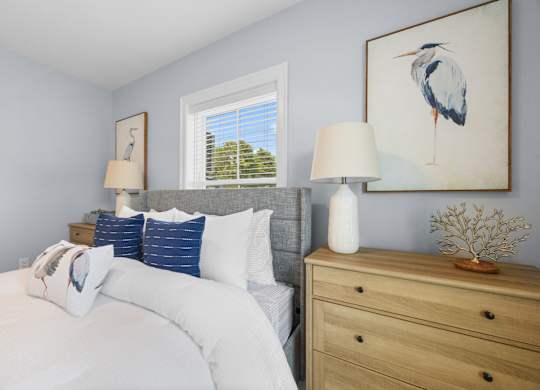 A bedroom with a bed, nightstand, and a painting of a bird on the wall.