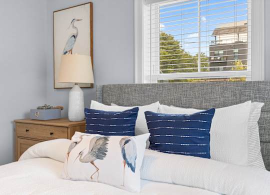 A bedroom with a bed, pillows, a nightstand, and a painting of a bird.