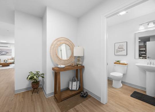A bathroom with a white toilet and sink, a mirror, and a wooden table with a plant on it.