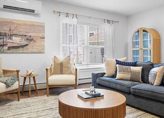 A living room with a blue couch, a wooden coffee table, and a painting of a harbor scene on the wall.