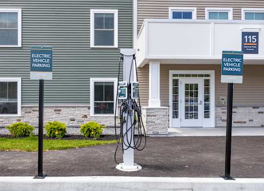 Two signs on a pole in front of a building that says Electric Vehicle Parking.