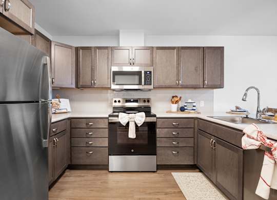 A kitchen with a refrigerator on the left and a stove top oven in the middle.