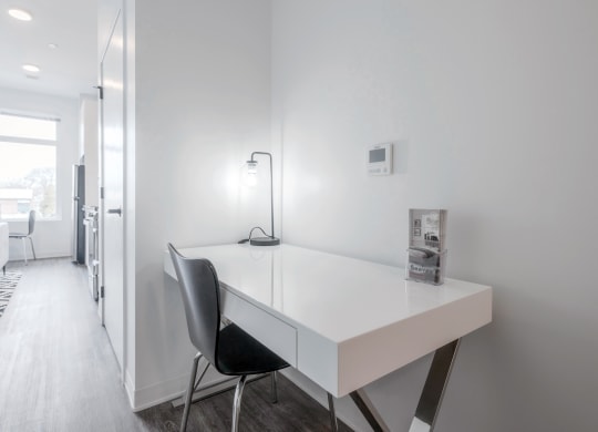 a white desk in a white room with a black chair