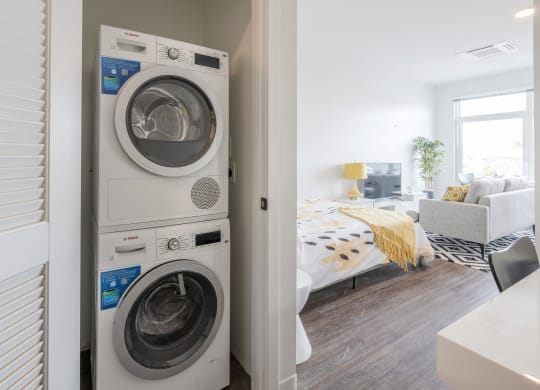 a front loading washer and dryer in a bedroom with a bed
