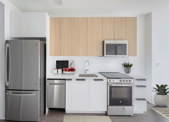 A modern kitchen with a refrigerator, microwave, oven, and sink.