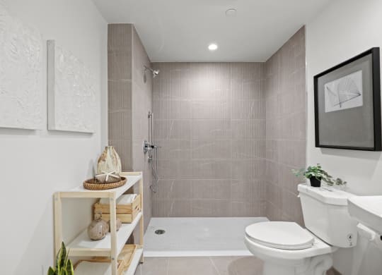 a bathroom with tiled walls and floor and a walk in shower with a glass door at The Fairfax Flats Apartments, Los Angeles, CA