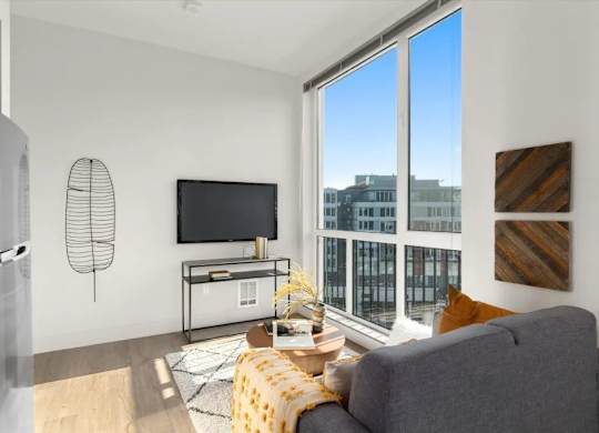 A living room with a grey couch, a television, and a window overlooking a cityscape.