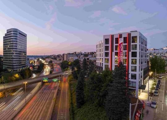 A cityscape with a highway and a tall building with a red banner on it.