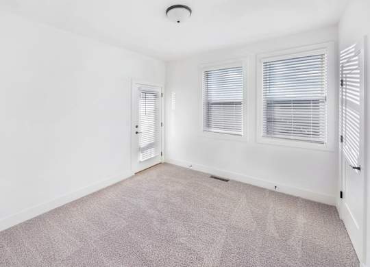 A room with a carpeted floor and two windows with blinds.