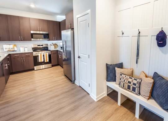 A kitchen with a refrigerator and a bench with pillows.
