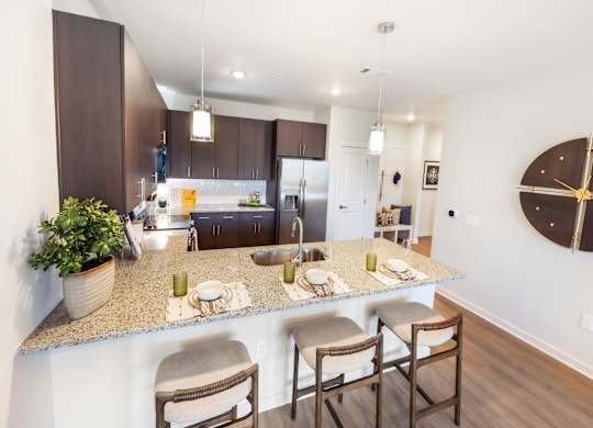 A kitchen with a counter and chairs in the foreground and a dining area in the background.