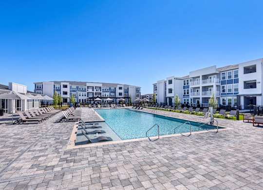 A large swimming pool surrounded by lounge chairs and buildings in the background.