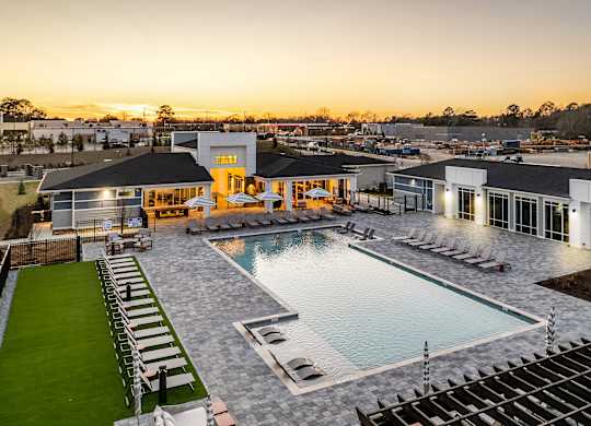 A large outdoor swimming pool surrounded by lounge chairs and a building with a yellow entrance.