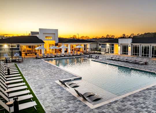A large outdoor swimming pool surrounded by lounge chairs and a building in the background.
