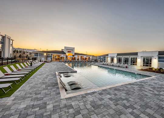 A swimming pool surrounded by a paved area and lounge chairs.