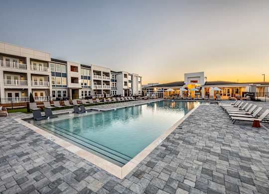 A large outdoor swimming pool surrounded by a stone patio and lounge chairs.