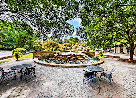 A patio with a table and chairs overlooking a fountain.