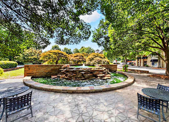 A fountain in the middle of a circular patio surrounded by trees.
