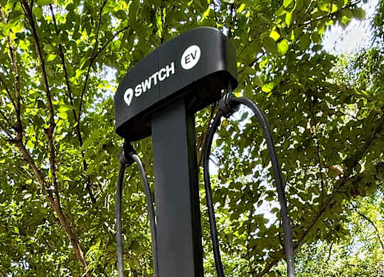 A black electric vehicle charging station with a green light on.