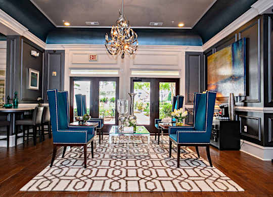A living room with a chandelier, two blue chairs, and a patterned rug.