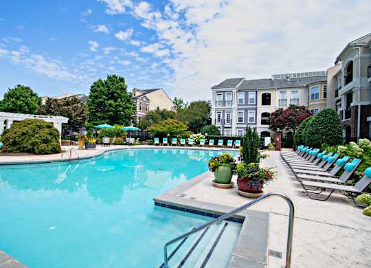 A large swimming pool surrounded by lounge chairs and potted plants.