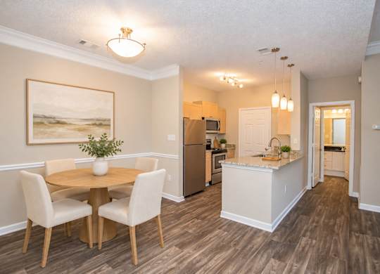 A dining room with a table and chairs and a kitchen in the background.