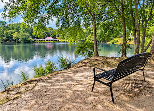 A black bench is on a hill overlooking a lake.