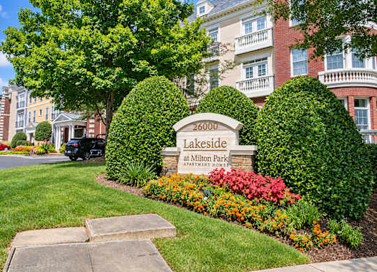 The image shows a beautiful lakeside apartment complex with a sign in front.
