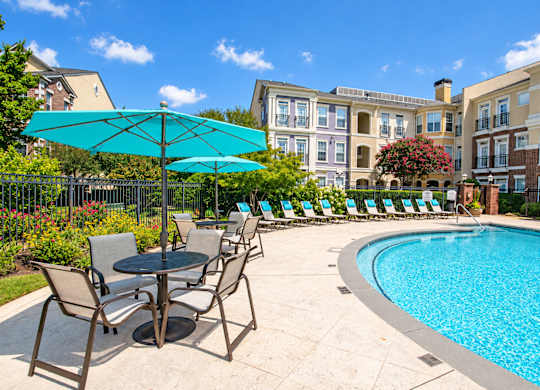 A pool area with chairs and umbrellas in front of a building.