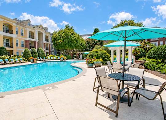 A pool area with a table and chairs and a blue umbrella.