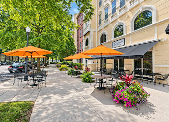 A city sidewalk with tables and chairs and umbrellas.