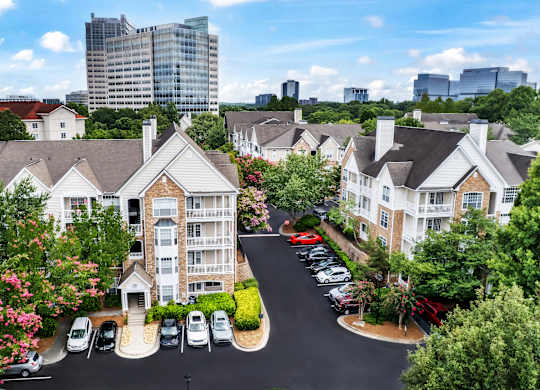 A view of a residential area with apartment buildings, cars parked in a lot, and trees.