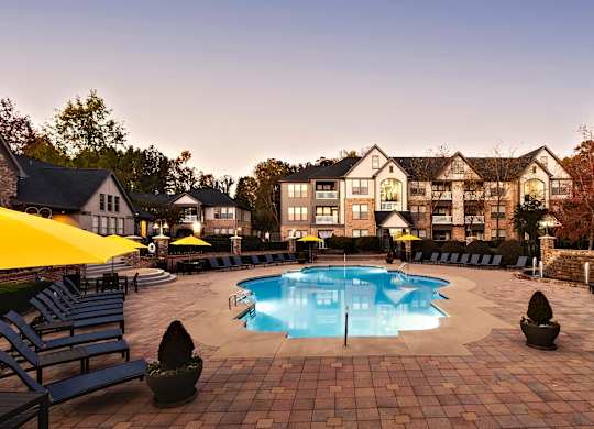 A large swimming pool surrounded by lounge chairs and umbrellas in front of a building.