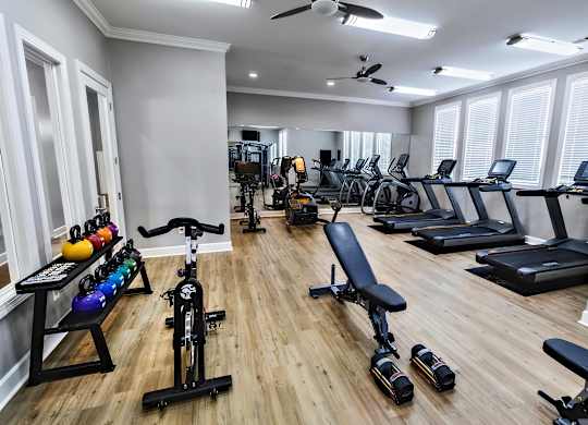 A well-lit gym with a variety of equipment including treadmills, stationary bikes, and weight machines.