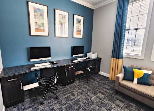 A room with a blue wall and a desk with two computers on it.