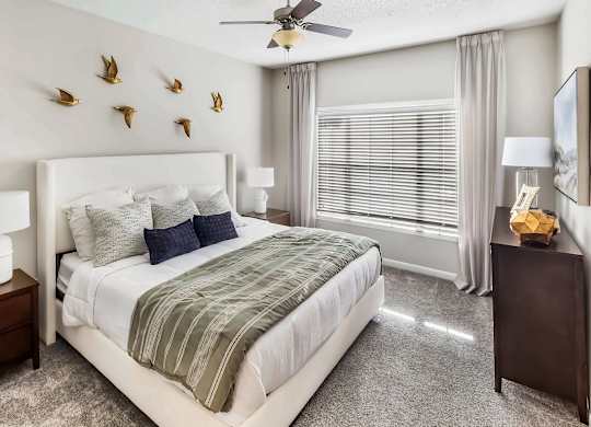 A bedroom with a large bed, a ceiling fan, and a wall decoration of birds.