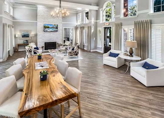 A large, well-lit living room with a wooden table and white chairs.