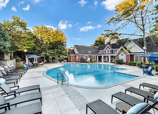 A large outdoor swimming pool surrounded by lounge chairs and trees.