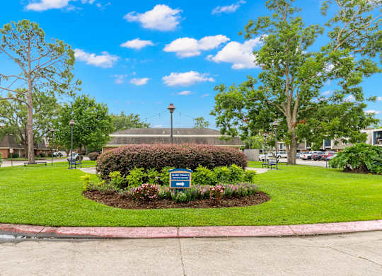 A sign in a grassy area with a tree and a building in the background.
