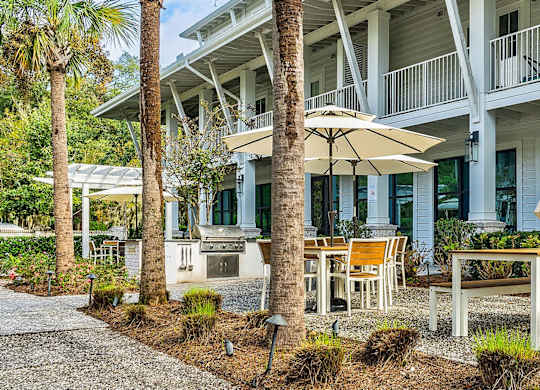 A white building with a balcony and a patio with chairs and an umbrella.
