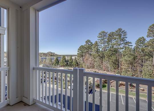 A balcony with a view of a parking lot and trees.