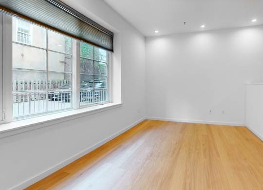 A room with wooden flooring and a window overlooking a building.