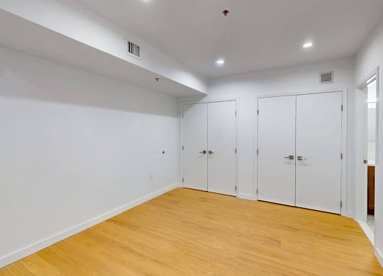 A room with white walls and wooden flooring with three white doors.