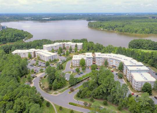 A large white building complex is surrounded by trees and a body of water.